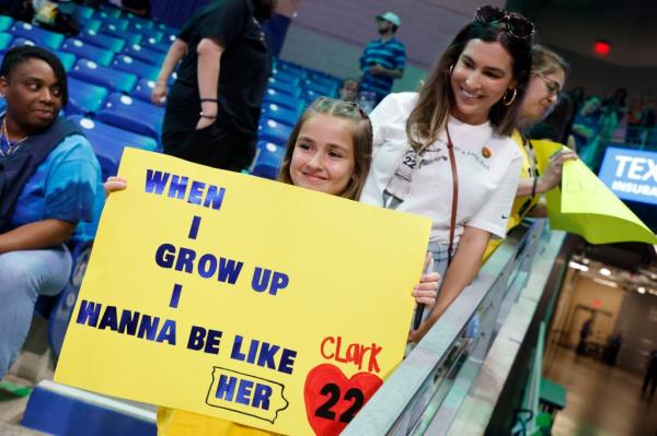 Pailynn Amos, center, holds a sign for Indiana Fever guard Caitlin Clark in front of her mother Rebecca Amos, of Ennis, Texas, prior to an WNBA basketball game against the Dallas Wings in Arlington, Texas, Friday, May 3, 2024. 