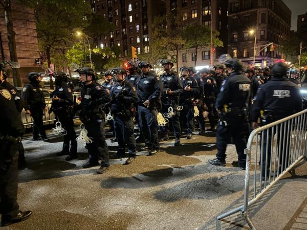 Approximately 50 NYPD officers in riot gear mobilizing at an intersection near Columbia protests